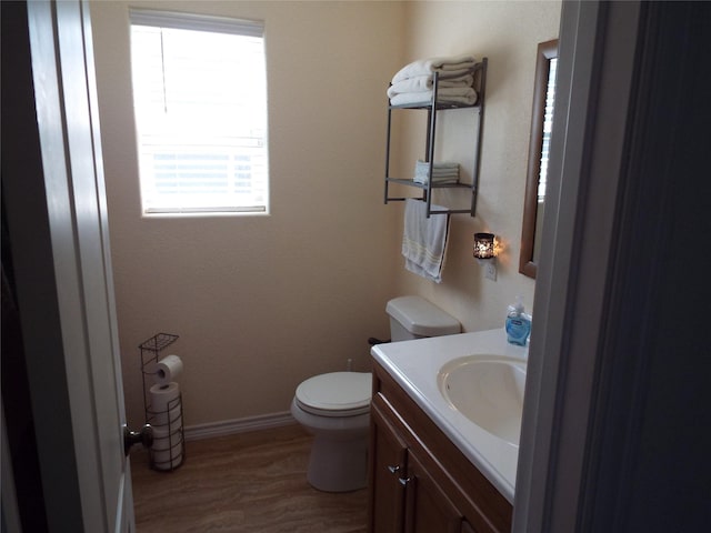 half bathroom with toilet, vanity, wood finished floors, and baseboards