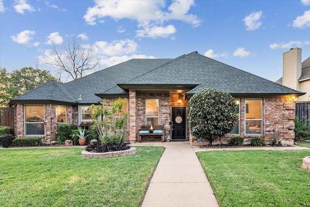 view of front of home with brick siding, a shingled roof, a front yard, and fence