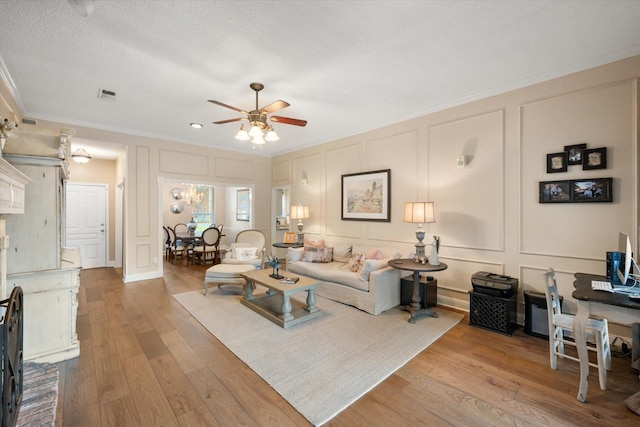living room with a ceiling fan, visible vents, ornamental molding, and a decorative wall