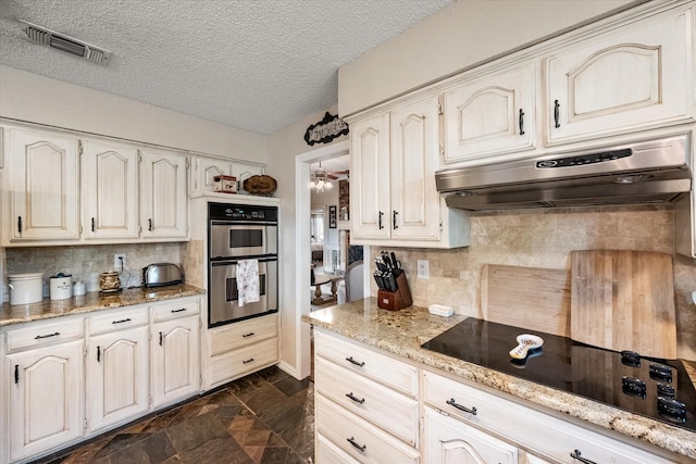 kitchen with black electric cooktop, double oven, under cabinet range hood, visible vents, and decorative backsplash
