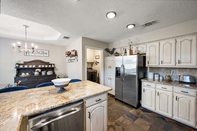 kitchen with stainless steel appliances, a textured ceiling, visible vents, an inviting chandelier, and washer / dryer
