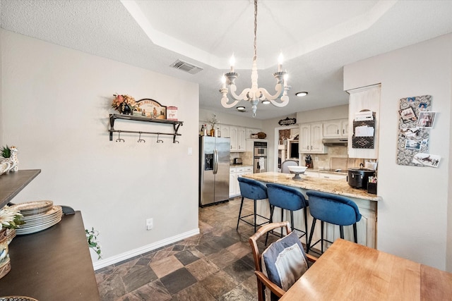 kitchen featuring a breakfast bar area, an inviting chandelier, stainless steel appliances, a peninsula, and visible vents