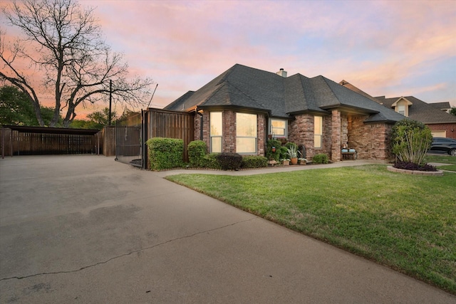 french provincial home featuring driveway, a gate, a yard, and brick siding