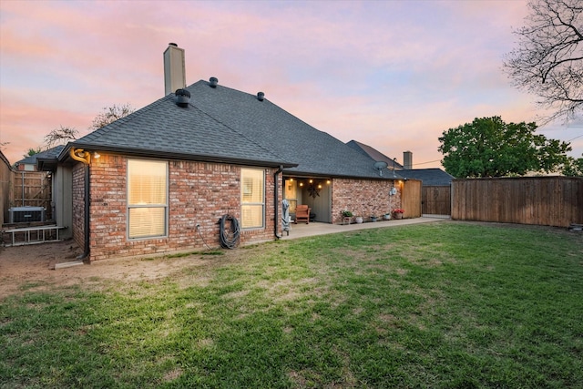 back of house featuring brick siding, a lawn, a shingled roof, and a fenced backyard