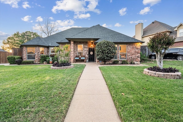 view of front of house with brick siding, a shingled roof, a front yard, and fence