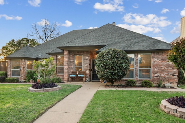 view of front of house featuring brick siding, roof with shingles, and a front yard
