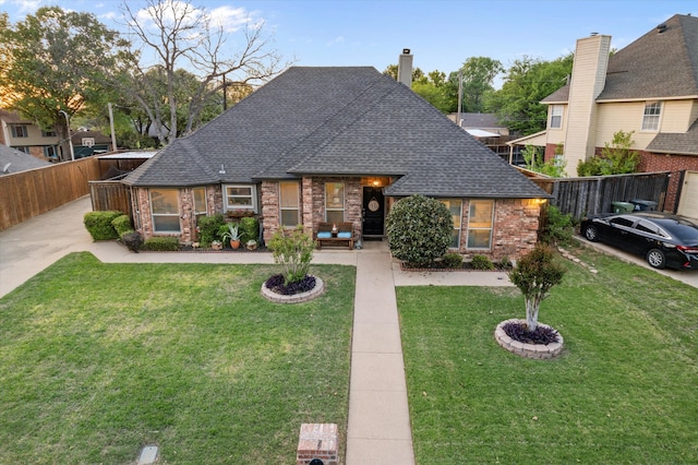 view of front of house featuring brick siding, roof with shingles, a front yard, and fence