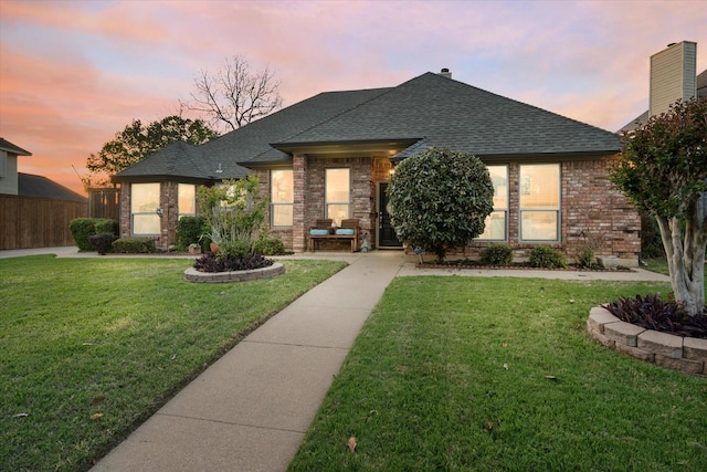view of front of house with brick siding, a front lawn, fence, and a shingled roof