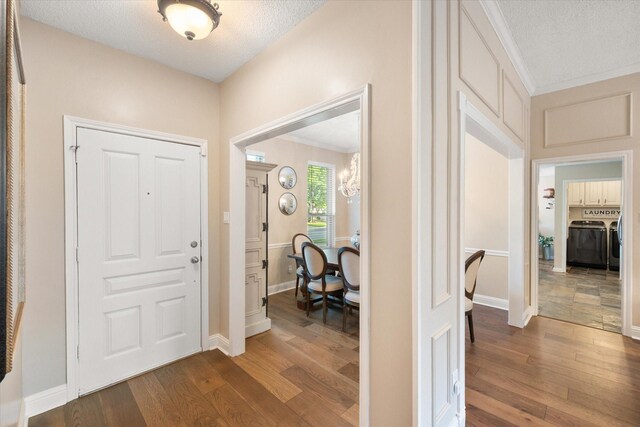 entrance foyer with dark wood finished floors, washing machine and dryer, ornamental molding, and a textured ceiling