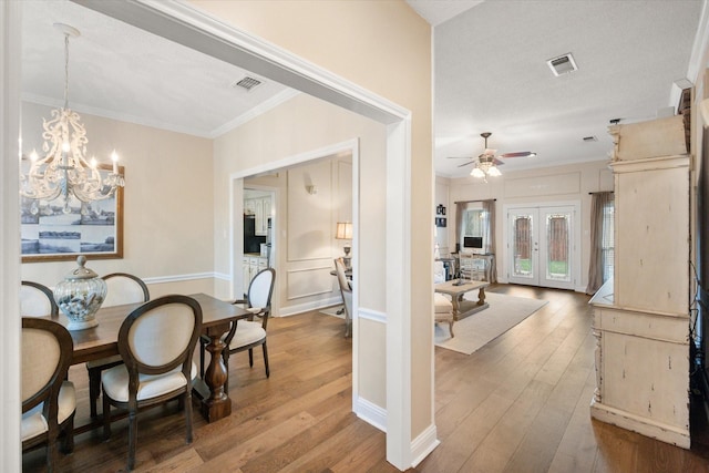 dining area featuring wood-type flooring, ornamental molding, visible vents, and ceiling fan with notable chandelier
