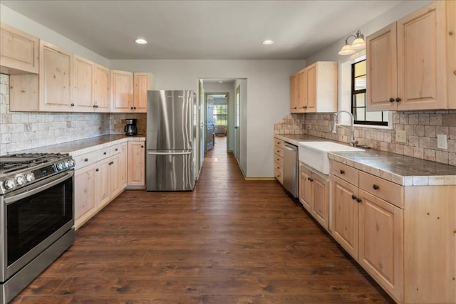 kitchen with stainless steel appliances, light brown cabinetry, a sink, dark wood-style floors, and backsplash