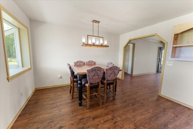 dining room featuring baseboards, wood finished floors, arched walkways, and a chandelier