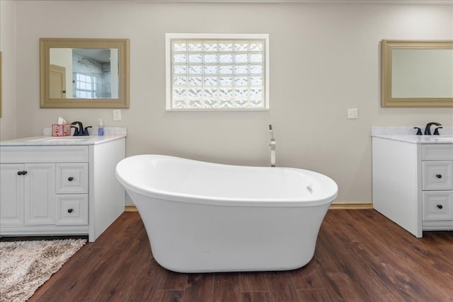 bathroom featuring two vanities, wood finished floors, a sink, and a freestanding bath
