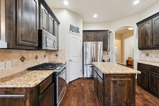 kitchen featuring arched walkways, dark brown cabinets, dark wood-style flooring, and stainless steel appliances