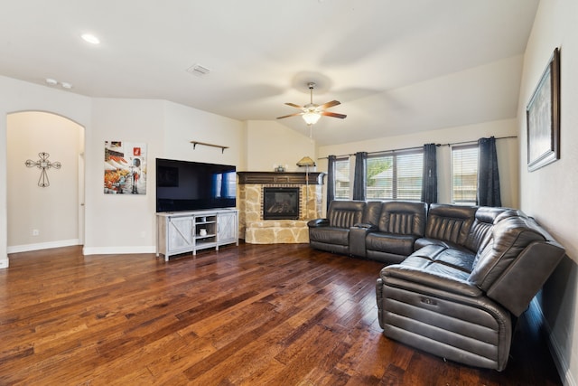 living area featuring a stone fireplace, arched walkways, baseboards, hardwood / wood-style flooring, and ceiling fan