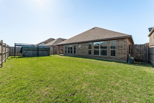 back of house featuring a fenced backyard, brick siding, and a lawn
