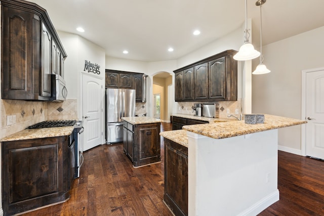 kitchen with dark wood-style floors, arched walkways, dark brown cabinetry, a peninsula, and appliances with stainless steel finishes