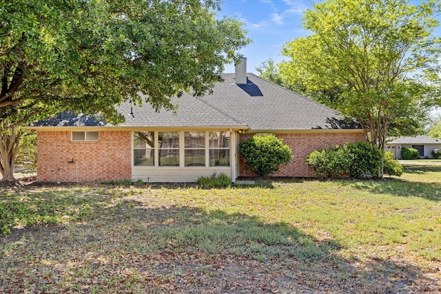 back of property featuring a lawn, a chimney, a shingled roof, and brick siding