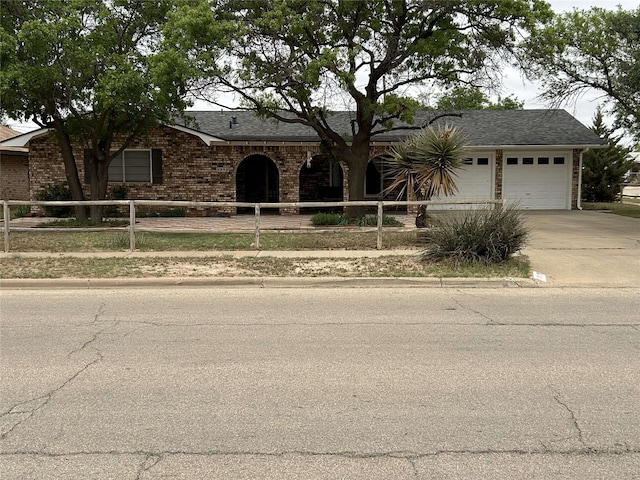 ranch-style house featuring a fenced front yard, a shingled roof, concrete driveway, an attached garage, and brick siding