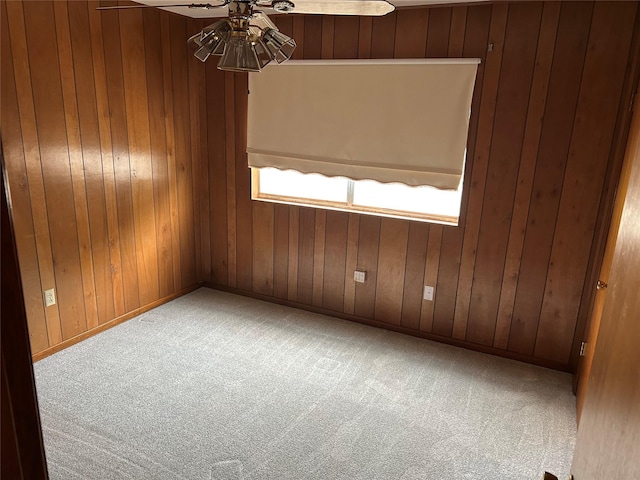 empty room featuring carpet floors, a ceiling fan, baseboards, and wood walls