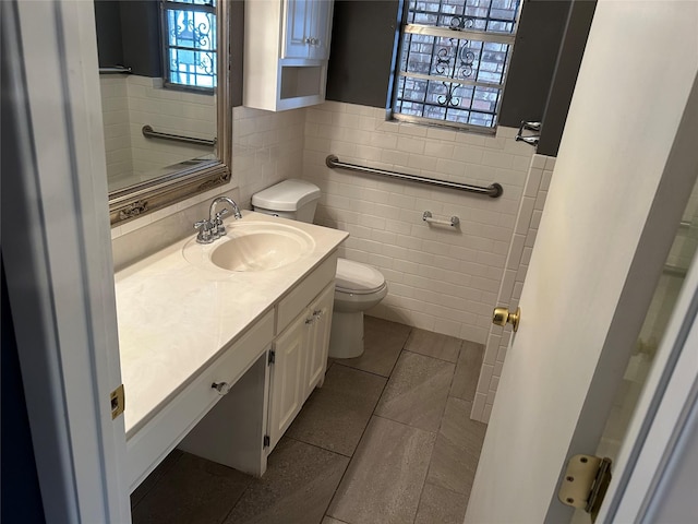 bathroom featuring tile patterned floors, toilet, tile walls, wainscoting, and vanity