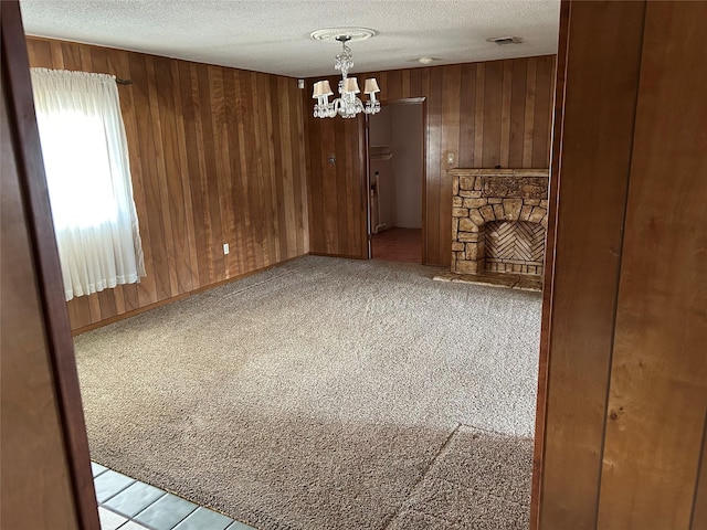 interior space with a textured ceiling, carpet, an inviting chandelier, wood walls, and a stone fireplace