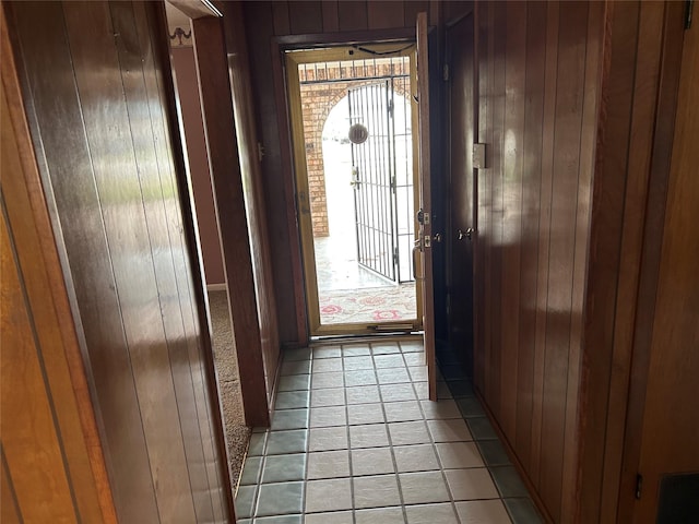 doorway with wood walls and light tile patterned floors