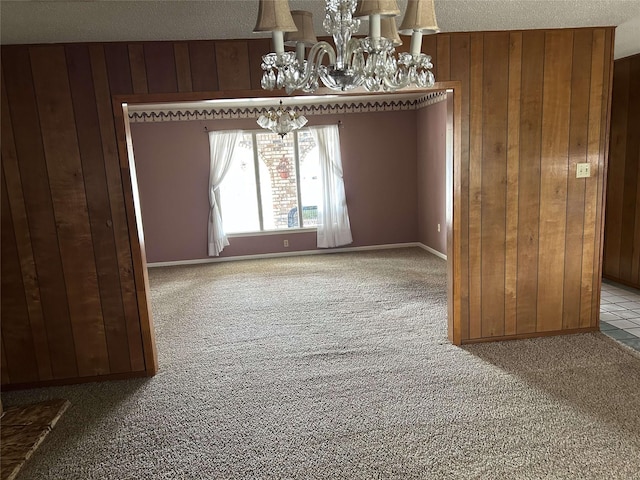 unfurnished dining area featuring wood walls, carpet flooring, a chandelier, and a textured ceiling