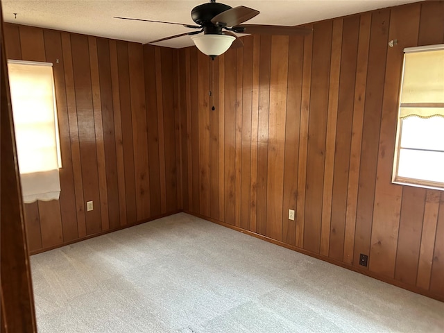 empty room with light colored carpet, ceiling fan, and wood walls