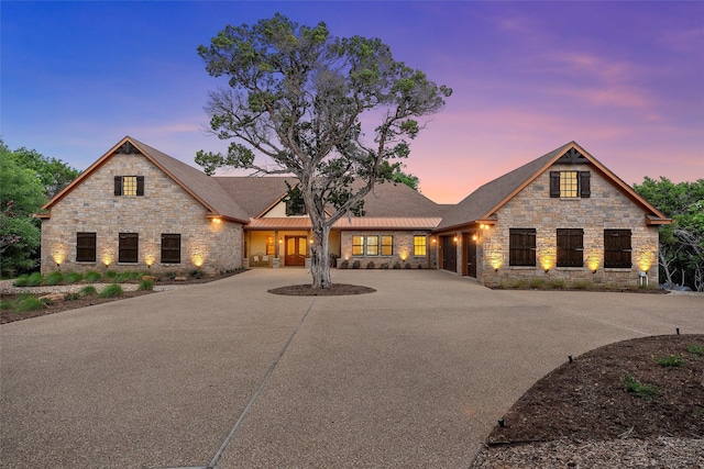 french country style house with an attached garage, stone siding, and curved driveway