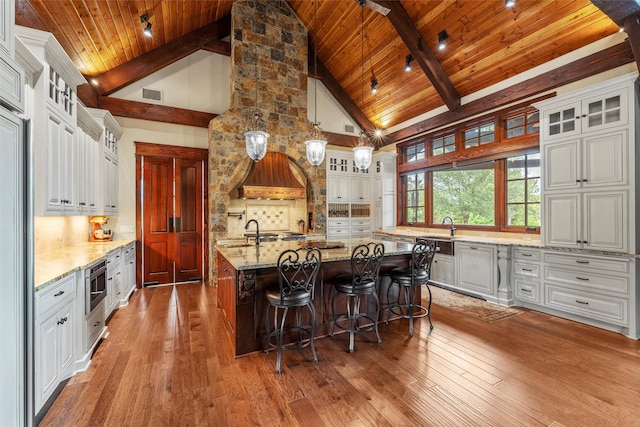kitchen featuring beamed ceiling, wooden ceiling, an island with sink, and wood-type flooring