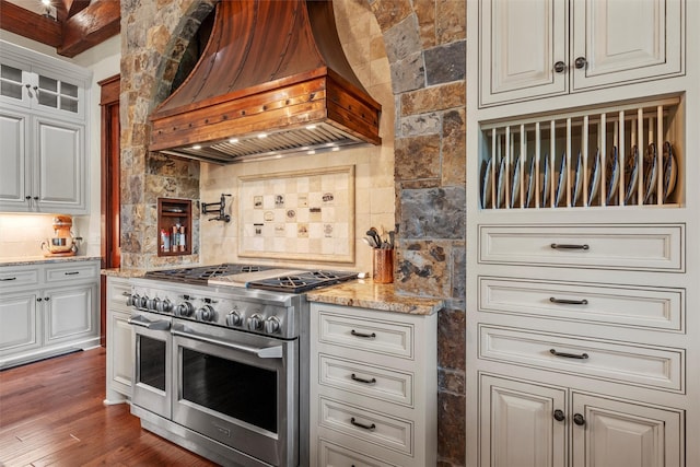 kitchen with decorative backsplash, light stone countertops, double oven range, and custom range hood