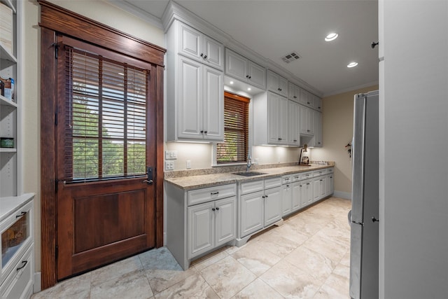 kitchen with white cabinets, crown molding, a sink, and visible vents