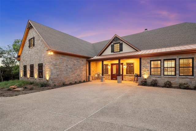 view of front facade with stone siding, a shingled roof, a porch, metal roof, and a standing seam roof