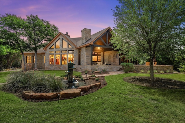 back of property with a lawn, a chimney, and stone siding