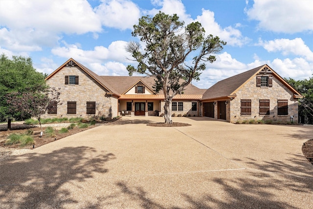 view of front of home with a standing seam roof, driveway, stone siding, metal roof, and an attached garage
