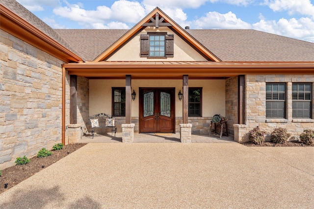 doorway to property featuring a shingled roof, stucco siding, french doors, covered porch, and stone siding