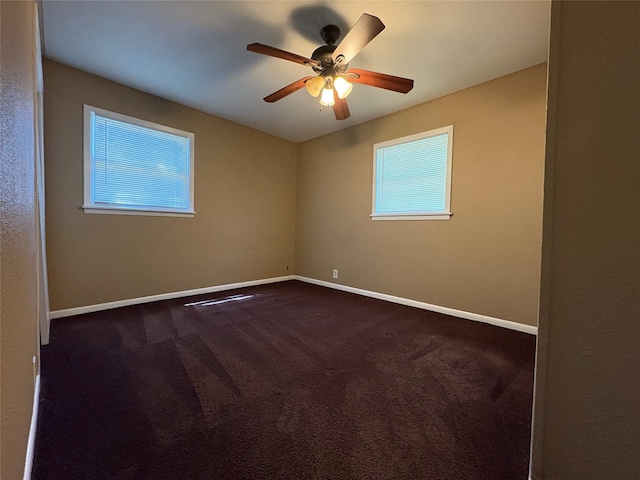 empty room with ceiling fan, a wealth of natural light, dark colored carpet, and baseboards