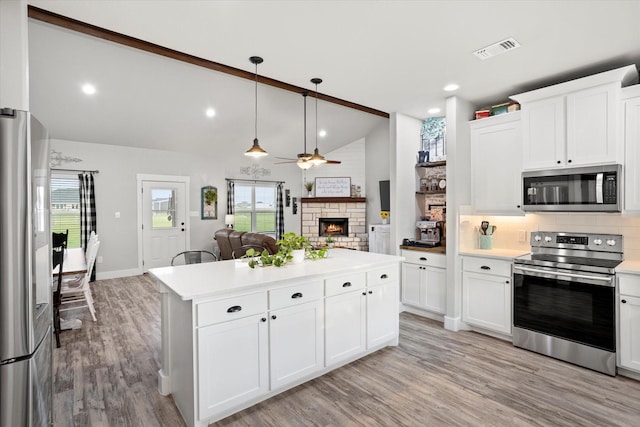 kitchen featuring ceiling fan, appliances with stainless steel finishes, a fireplace, light countertops, and visible vents