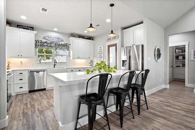 kitchen with a center island, tasteful backsplash, a sink, light wood finished floors, and appliances with stainless steel finishes