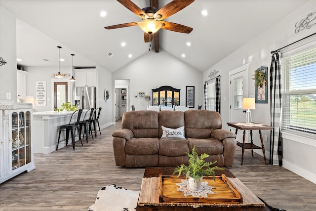living area with vaulted ceiling with beams, ceiling fan, baseboards, and light wood-style flooring