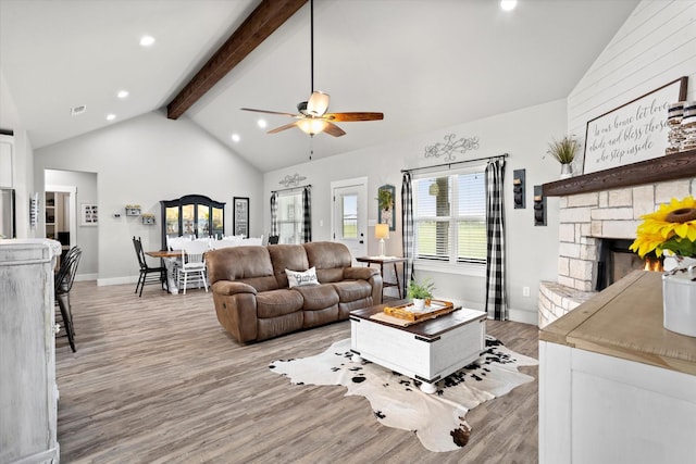 living area featuring beam ceiling, a fireplace, high vaulted ceiling, light wood-type flooring, and a ceiling fan