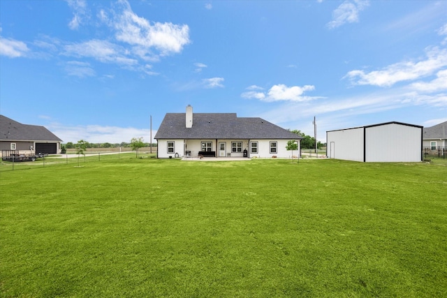 back of property featuring fence, a patio, a yard, a chimney, and an outbuilding