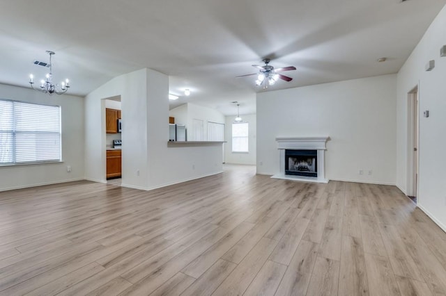 unfurnished living room with ceiling fan with notable chandelier, visible vents, light wood-style floors, and a fireplace with raised hearth