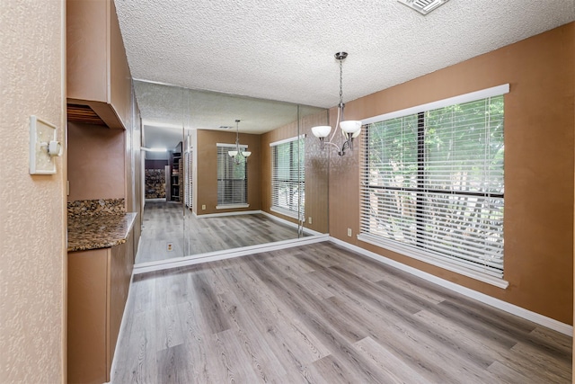 1201 Harwell Dr Unit 225, Arlington, TX 76011 - unfurnished dining area featuring light wood-style flooring, a textured ceiling, a chandelier, and baseboards