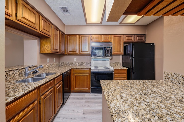 1201 Harwell Dr Unit 225, Arlington, TX 76011 - kitchen featuring black appliances, a sink, brown cabinetry, light wood-style flooring, and light stone counters