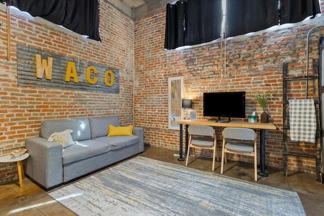 living area with concrete flooring, a towering ceiling, and brick wall