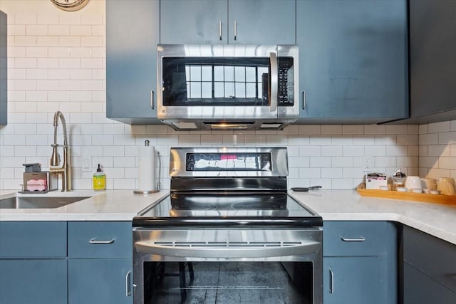kitchen with tasteful backsplash, a sink, stainless steel appliances, light countertops, and blue cabinetry