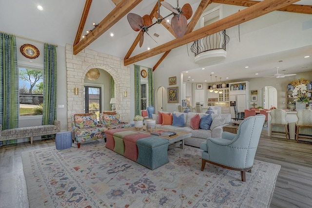 living room featuring arched walkways, beamed ceiling, a ceiling fan, wood finished floors, and high vaulted ceiling