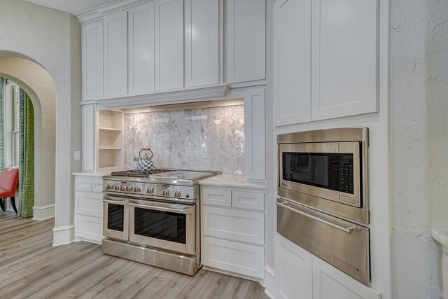 kitchen with stainless steel appliances, light wood-type flooring, white cabinetry, a textured wall, and light countertops